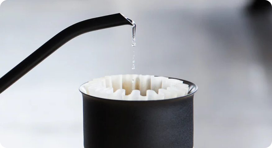 A kettle pours water into a coffee filter in a black coffee dripper for the home barista.