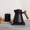 Sleek black electric kettle with wooden handle for the perfect home barista coffee setup.