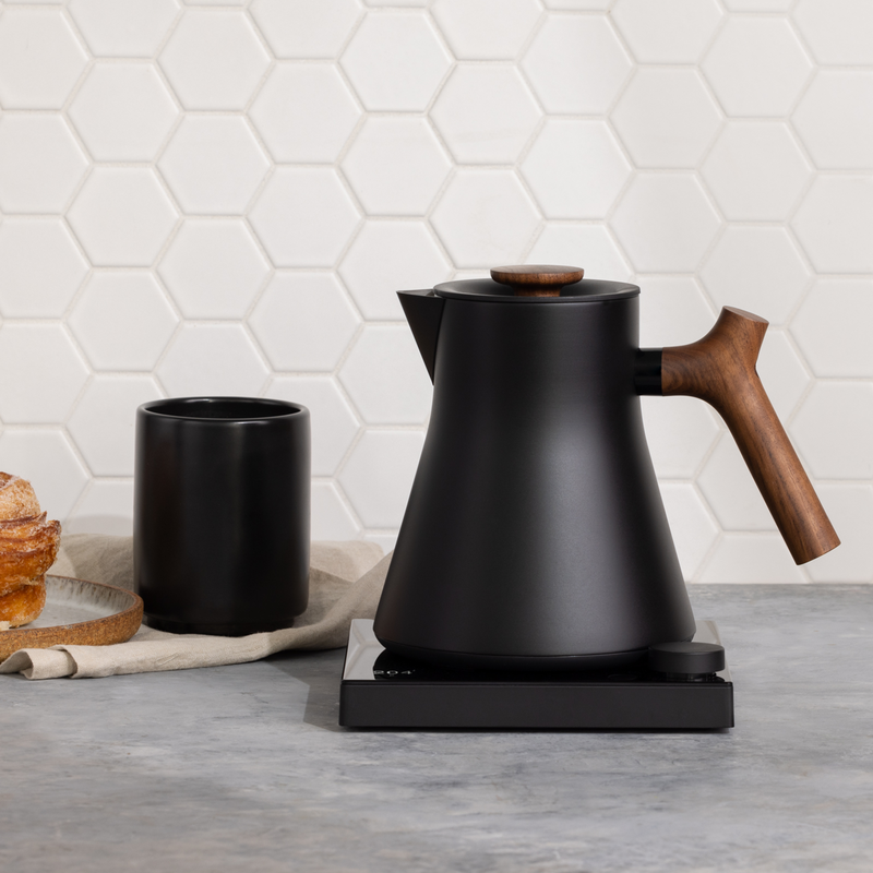 Sleek black electric kettle with wooden handle for the perfect home barista coffee setup.