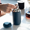 Stone blue carter move mug showing snap in splash guard with lid on side of table.