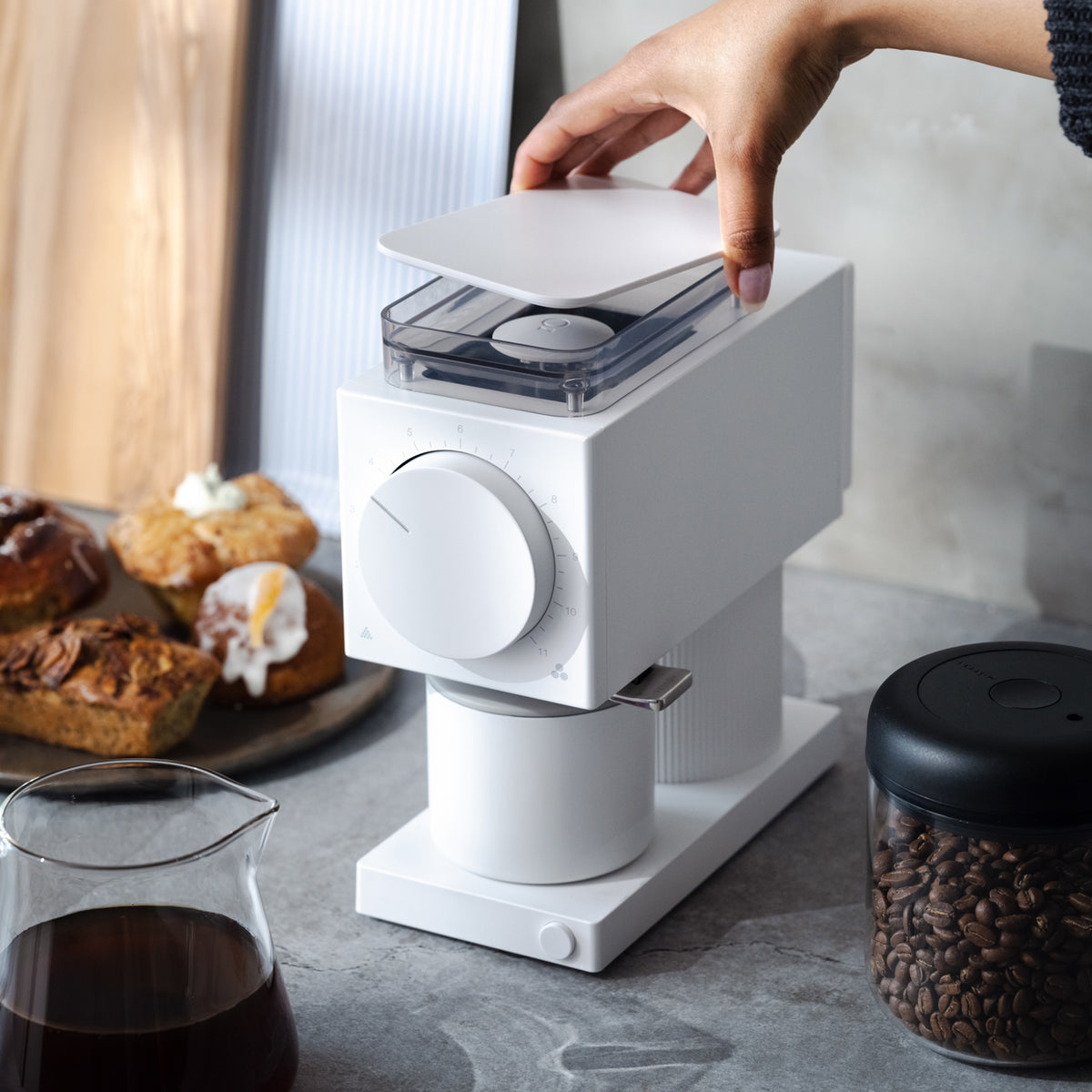 A home barista operates a modern white coffee grinder on a kitchen counter with pastries.