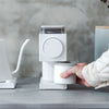 A home barista holds a white cup under a modern coffee grinder on a gray countertop.