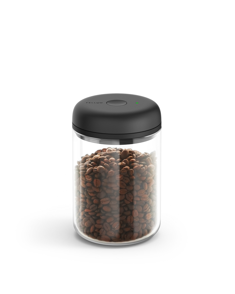 Fellow Atmos Vacuum Canister with black lid, filled with coffee beans on a white background.