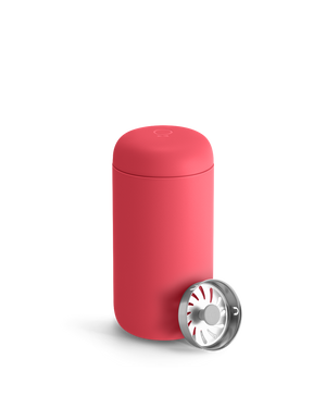 A Coral Crush Fellow Carter Move Mug with a metallic lid sits in front.