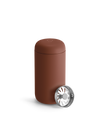 Fellow Carter Move Mug with lid next to a metal part with radial openings.