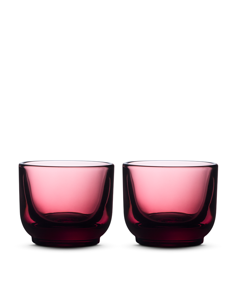 Two Pirch Espresso Glasses by Fellow in transparent dark pink sit side by side on a light background.