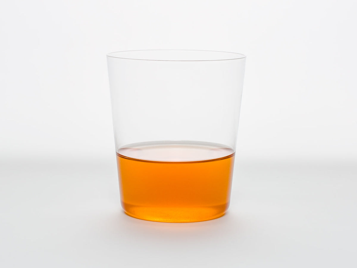 A clear glass half-filled with Song Tea & Ceramics Carrot tea on a white background.