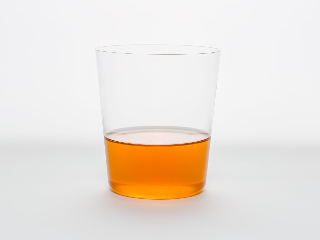 A clear glass half-filled with Song Tea & Ceramics Carrot tea on a white background.